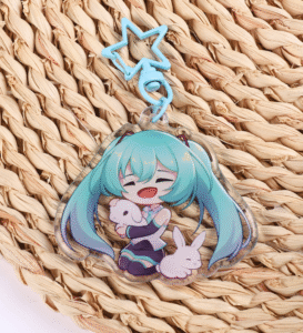 An acrylic keychain with a blue star clasp, sitting on top of a woven decor piece. The character featured on the keychain has long blue hair, and she's holding a white bunny in her arms. There's another bunny sleeping beside her.